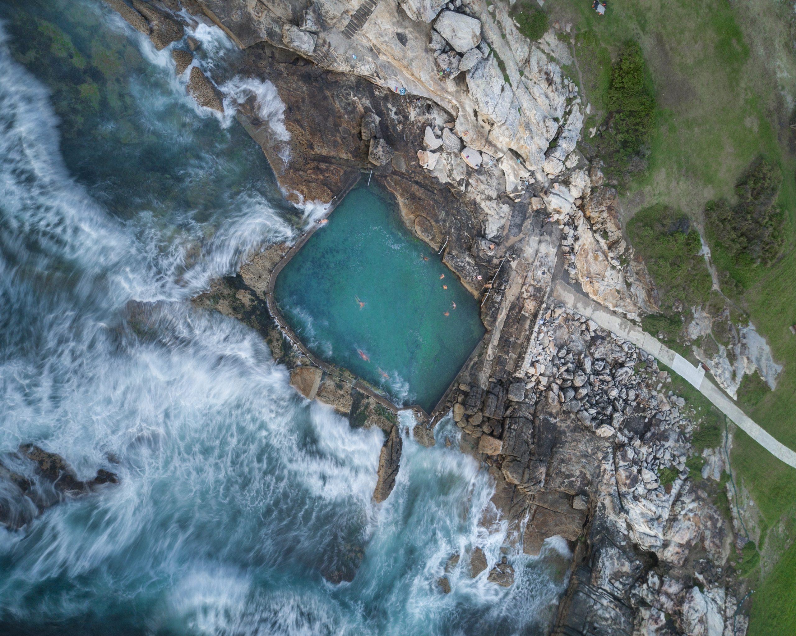 aerial shot of people swimming in a large pool built on the rocky coast in thailand